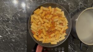 Dodavanje testenine u sos od pečene paprike i kobasice.